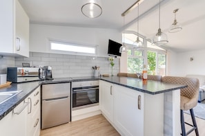A modern kitchen with a built-in oven, microwave, and coffee maker, a large island with seating, and pendant lighting.