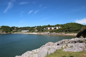 A coastal view with a rocky shoreline, a calm sea, and buildings on a hillside.