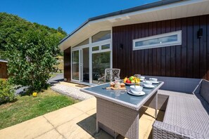 A modern outdoor dining area with a table set for two, surrounded by wicker furniture.