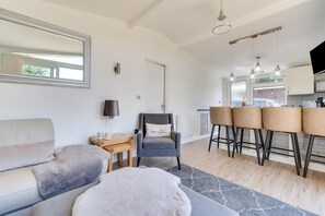 A modern living room with a sofa, a chair, a coffee table, and a kitchen area with bar stools.