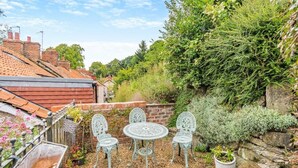 A patio with a table and chairs, surrounded by greenery and a brick wall. - 2 Bed in Pickering (oc-y114) (Pickering)