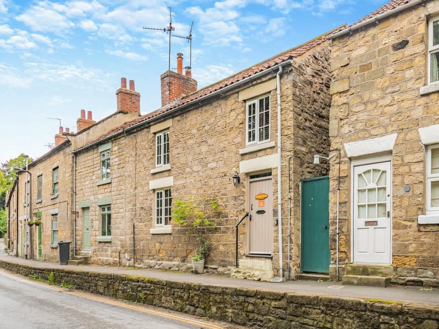 A row of stone buildings with traditional architecture, featuring multiple chimneys, windows with shutters, and a stone wall separating the properties.