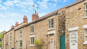 A row of stone buildings with traditional architecture, featuring multiple chimneys, windows with shutters, and a stone wall separating the properties. - 2 Bed in Pickering (oc-y114) (Pickering)