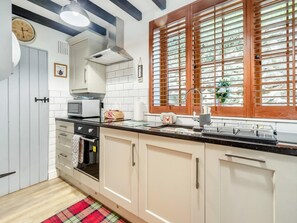 A kitchen with white cabinets, a microwave, a kettle, and a window with blinds.