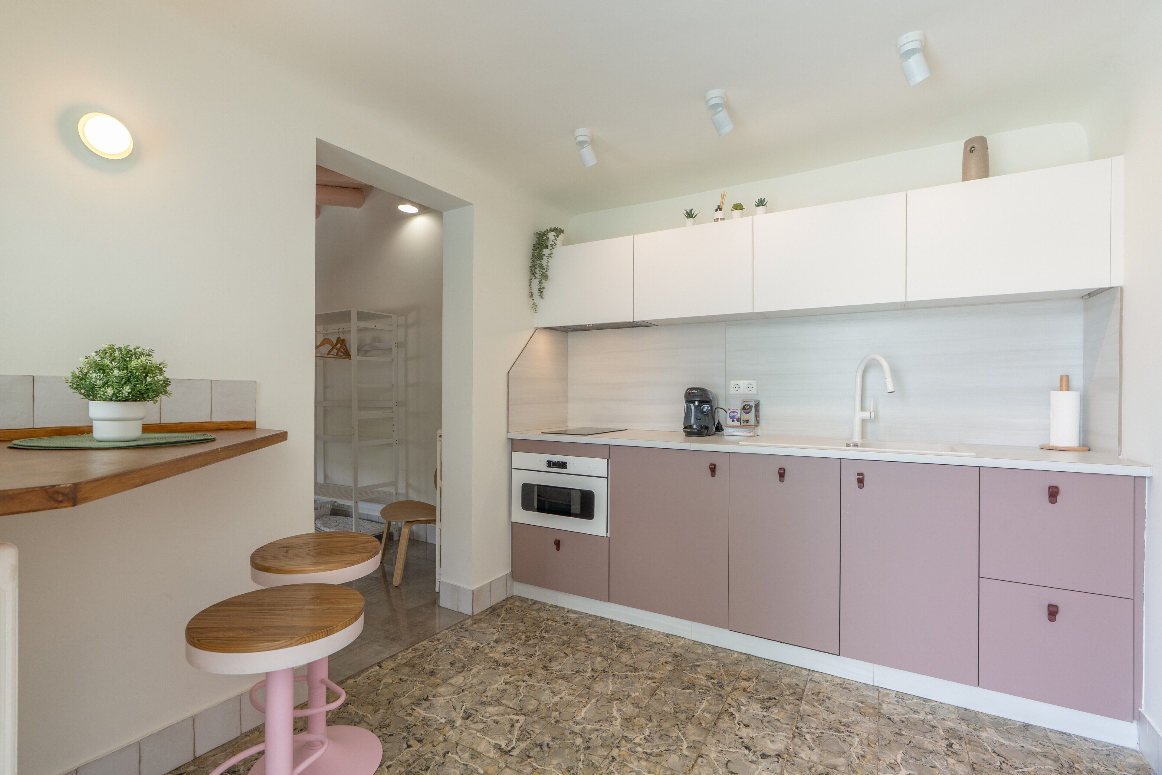 Una cocina moderna con encimera, lavabo, horno y alacenas. Hay dos taburetes y una planta en maceta.