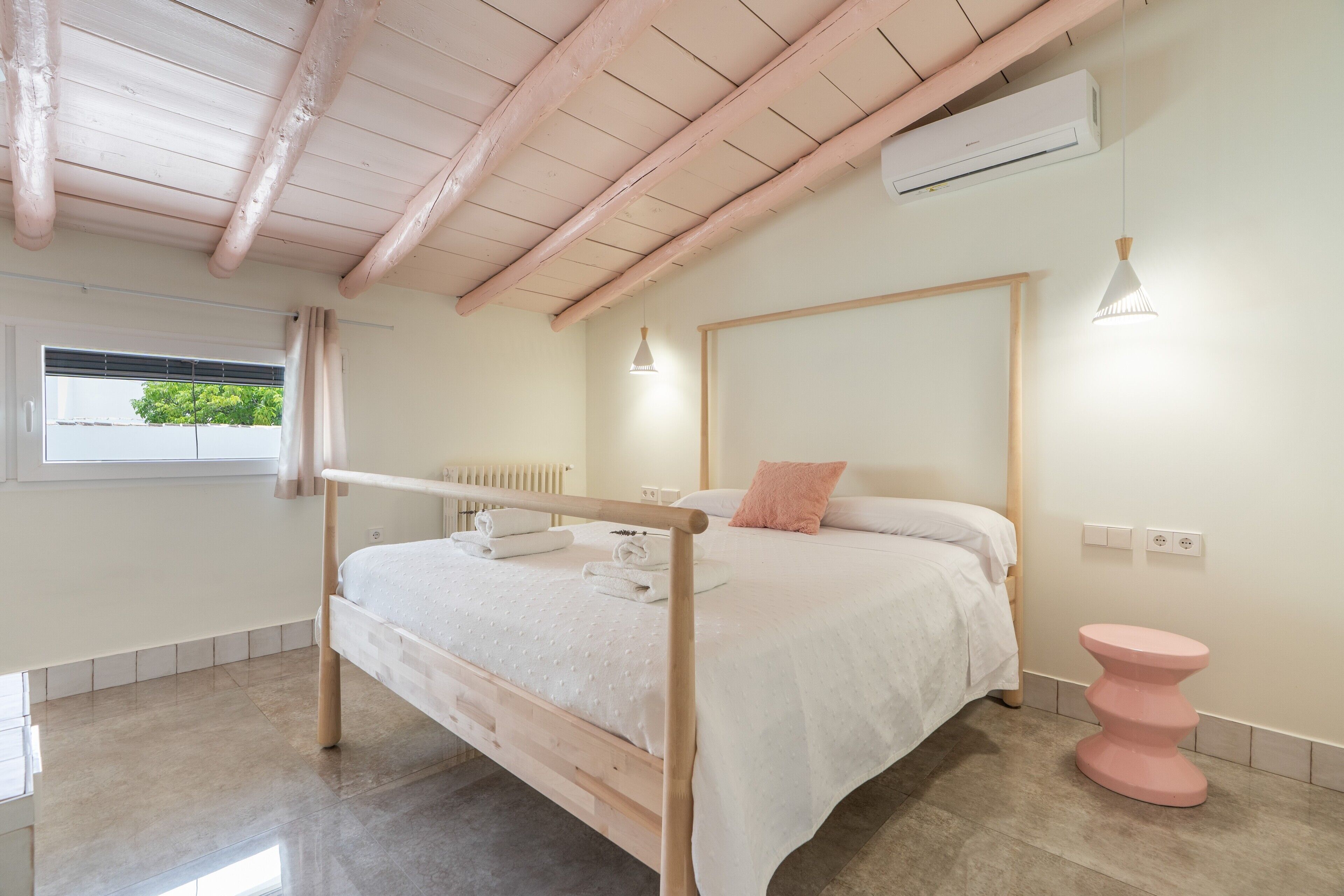 A bedroom with a wooden bed, a pink bedside table, a white radiator, and a window with curtains.