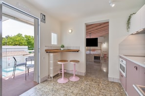 A kitchen with a countertop, two pink stools, a TV, and a view of a pool.