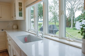 A kitchen with a large window, white cabinetry, and a sink. - Two-bedroom townhome in the heart of Saybrook Point with water/harbor views (Old Saybrook)