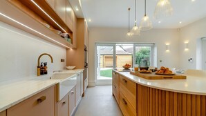 Une cuisine moderne dotée d’un îlot central aux lignes courbes, d’un éclairage suspendu et offrant une vue sur l’extérieur.