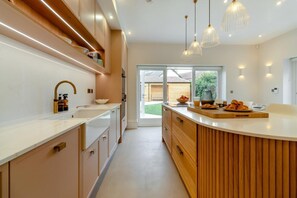 A modern kitchen with a curved island, pendant lighting, and a view to the outside. - 6 Bed in Southwold (oc-flgr) (Southwold)