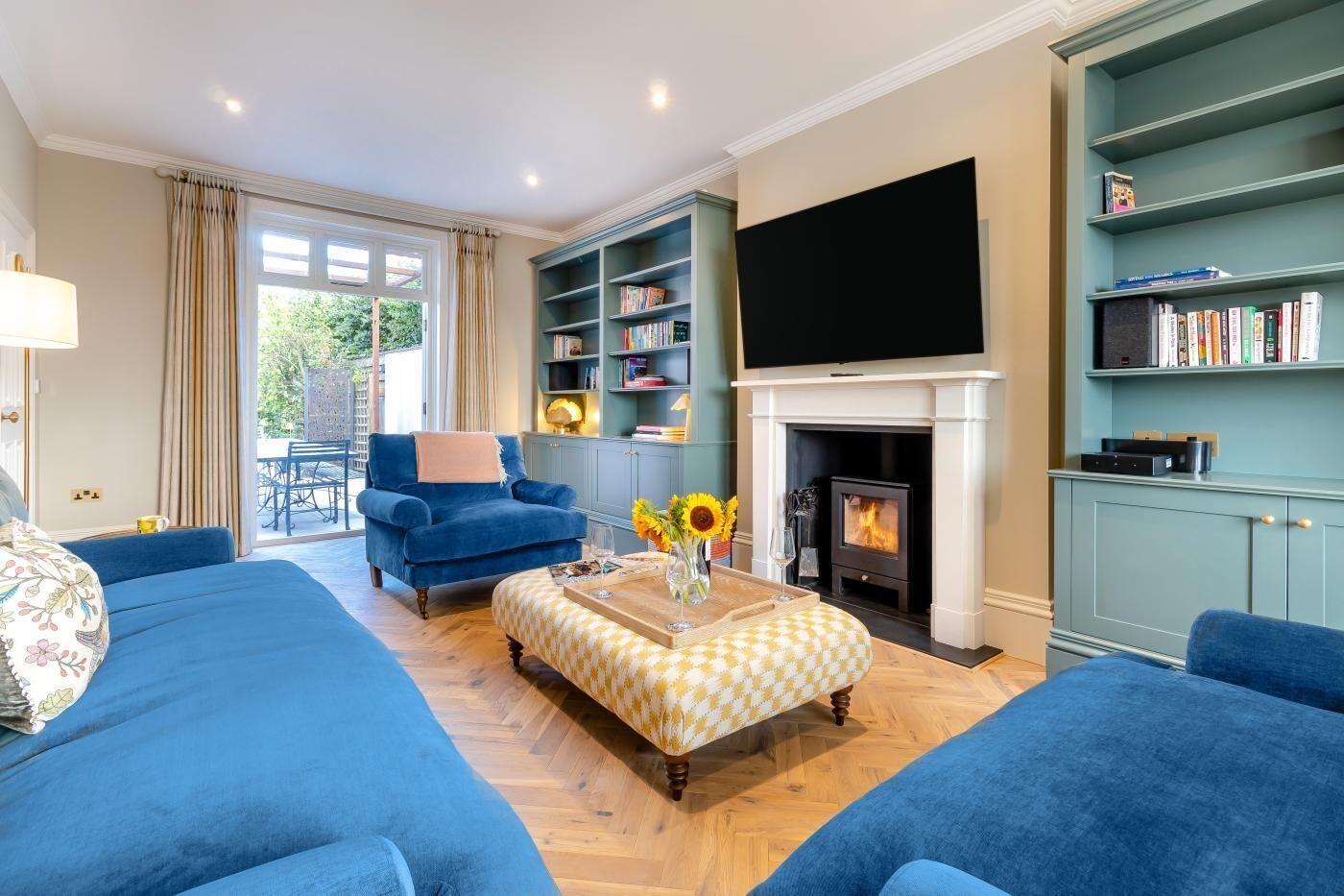 Ein Wohnzimmer mit Kamin, blauen Sofas, einem Bücherregal und einem Flachbildfernseher.