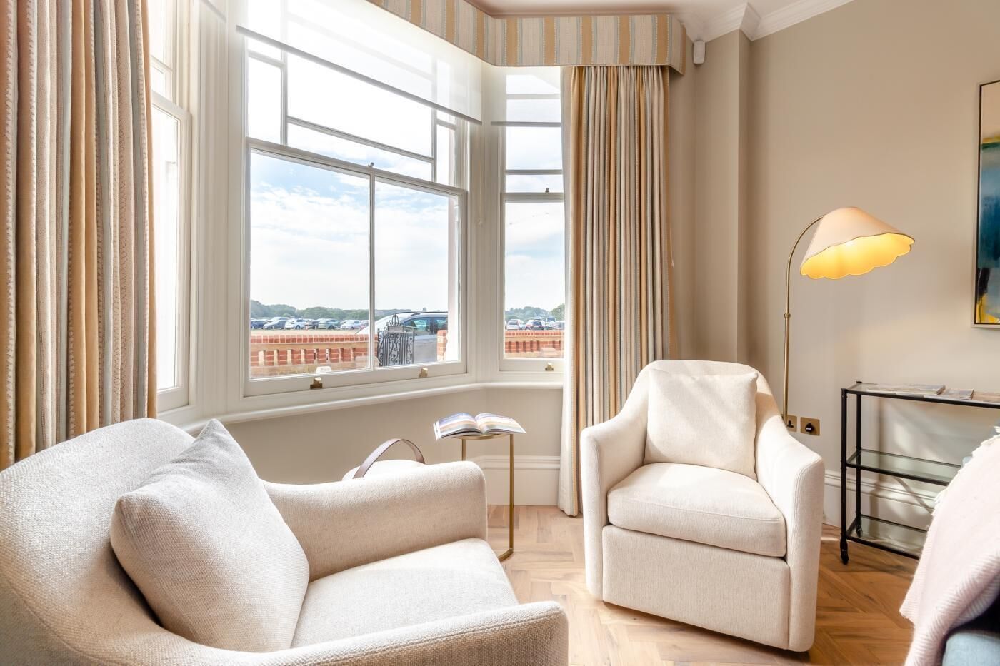 Une pièce avec deux fauteuils, un lampadaire et une vue sur un parking, visible à travers de grandes fenêtres.