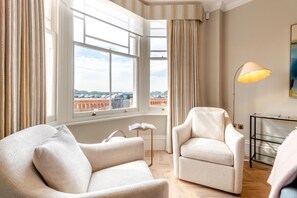 A room with two armchairs, a floor lamp, and a view of a parking lot through large windows. - 6 Bed in Southwold (oc-flgr) (Southwold)