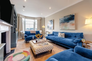 A modern living room with a blue sofa, a matching armchair, and a colorful woven rug. - 6 Bed in Southwold (oc-flgr) (Southwold)