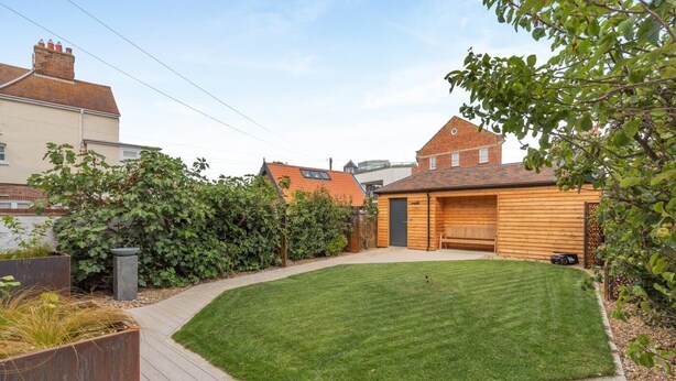 Un jardin bien entretenu avec une terrasse en bois, une pelouse et un abri de jardin en bois.