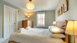 Un lit bien fait, avec des oreillers et des serviettes pliées, une lampe de chevet, une armoire en bois, un radiateur, une fenêtre avec vue et des œuvres d’art encadrées accrochées au mur.
