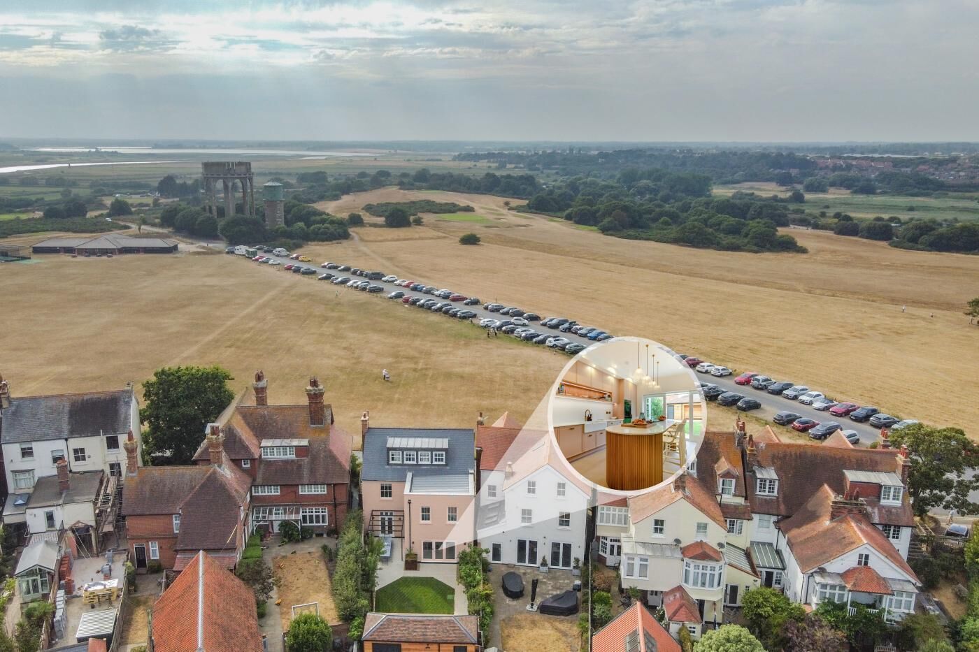 A residential area with a row of parked cars, a large open field, and a prominent tower structure in the distance.
