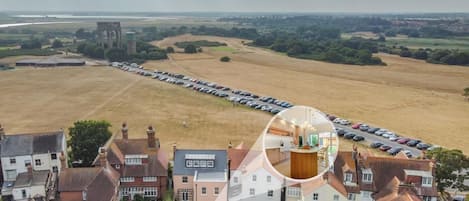 A residential area with a row of parked cars, a large open field, and a prominent tower structure in the distance.