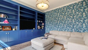 Un salon avec un meuble de rangement bleu pour l’équipement audiovisuel, un canapé beige et un papier peint à motifs.