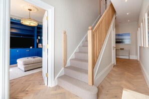 A staircase with a wooden handrail and carpeted steps leading to a room with a blue accent wall and a television. - 6 Bed in Southwold (oc-flgr) (Southwold)