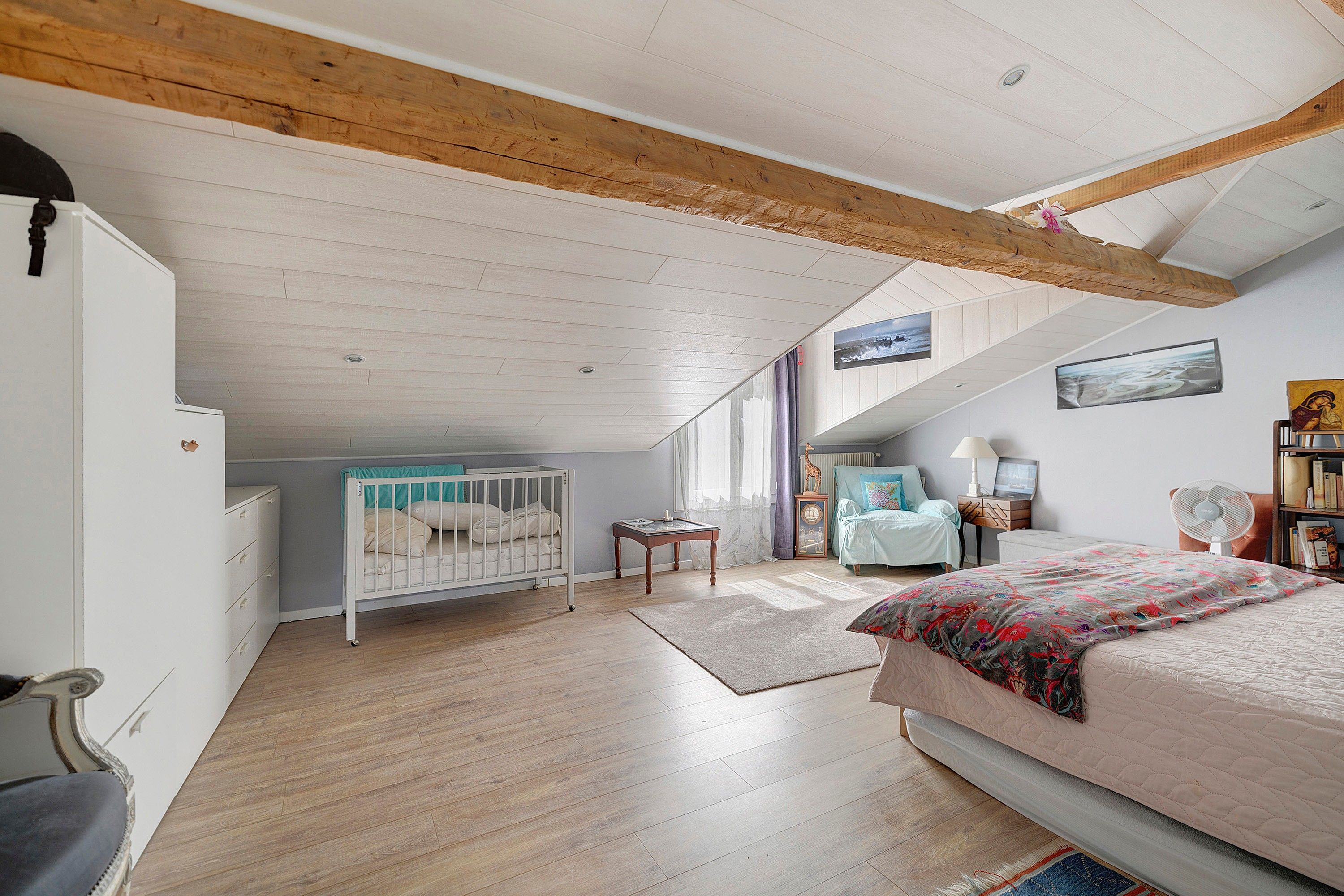 Ein Schlafzimmer mit schrägverdeckter Decke, einem Babybett, einem Bett, einer Kommode und einem Stuhl.