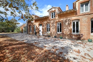 Un bâtiment traditionnel en briques, doté de nombreuses fenêtres et d’une allée gravillonnée.
