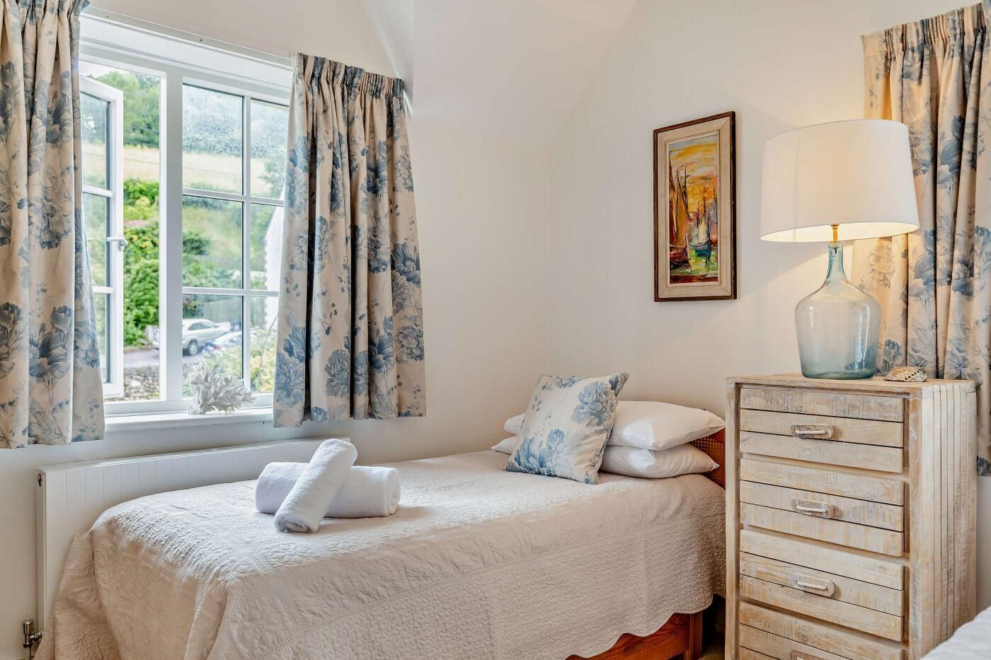 Une chambre à coucher avec un lit, une commode, une lampe et un tableau au mur.