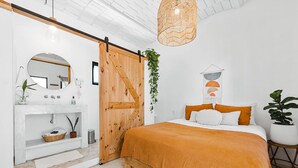 Ein Schlafzimmer mit einem Bett, einer Kommode, einem Spiegel, einer hängenden Pflanze und einer Schiebetür.