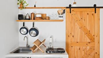 Een keuken met een spoelbak, twee koekenpannen, een waterkoker, een koffiezetapparaat, een theeset en een houten schuifdeur.