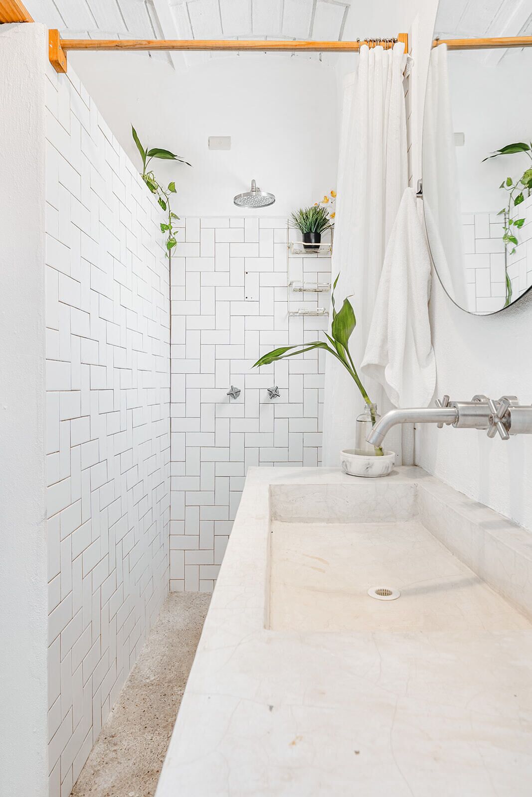 Un baño con ducha de azulejos blancos, lavabo con encimera de mármol y espejo con una toalla colgada.