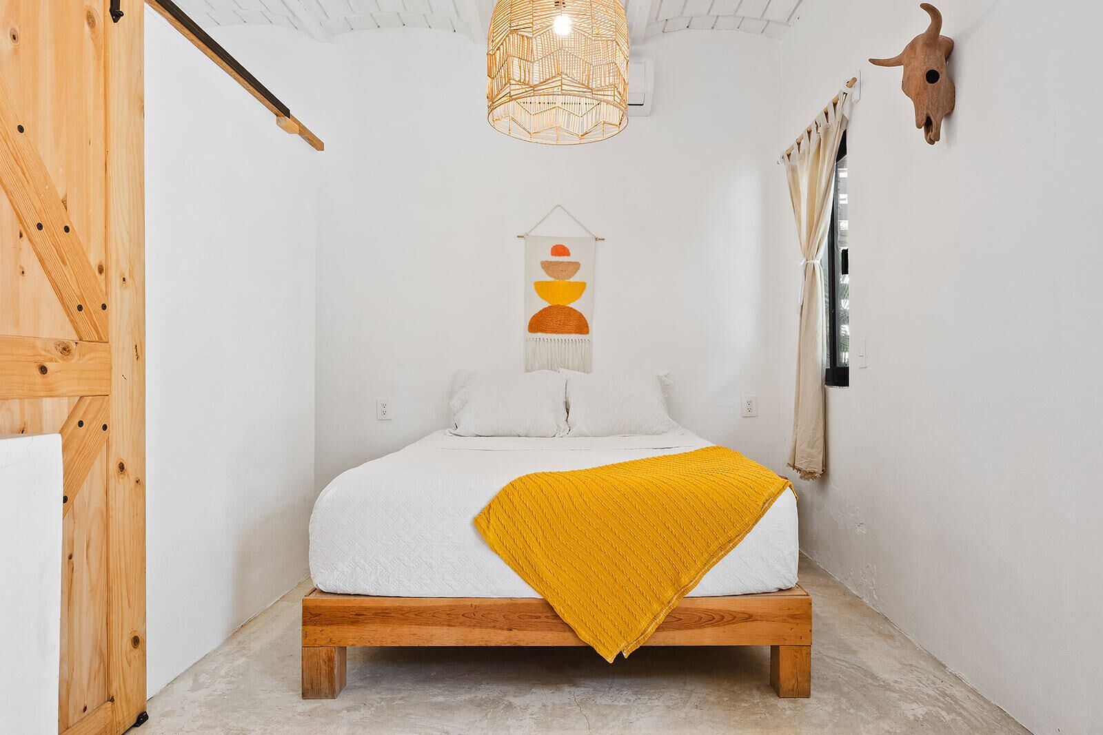 Un dormitorio con una cama de madera, una lámpara colgante, una decoración de cráneo de vaca montada en la pared y una obra de arte en la pared.