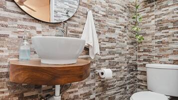 A bathroom with a round mirror, a wooden vanity, a white sink, a toilet, and a patterned wall.