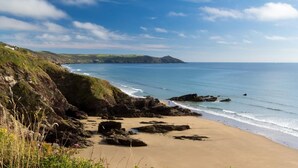 Un paisaje costero con una playa de arena, afloramientos rocosos y colinas cubiertas de hierba.