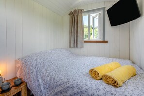 A bedroom with a bed, a window with curtains, a flat-screen TV mounted on the wall, and a bedside table with a lamp and bowls. - 1 Bed in St. Dominick (oc-h28184) (Saint Dominick)