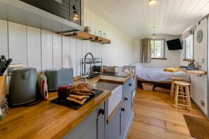 Cocina compacta con encimera de madera, lavamanos y barra de desayuno. Hay una cama con ventana y televisor montado en la pared.