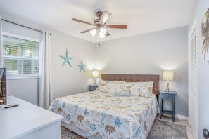 Een slaapkamer met een bed, twee nachtkastjes met lampen, een plafondventilator en decoratieve muursterren.