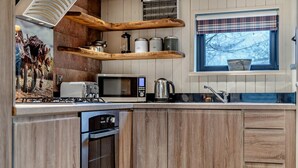 A kitchen with wooden cabinetry, a microwave, a kettle, and a window with a plaid curtain. - 2 Bed in Ash (oc-o29006) (Stoke Fleming)