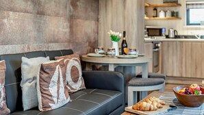 A modern living area with a sofa, a dining table with a bowl of fruit and croissants, and a kitchen in the background. - 2 Bed in Ash (oc-o29006) (Stoke Fleming)