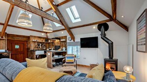 Een knusse woonkamer met een grote bank, een open haard en een keuken met houten balken en een dakraam.