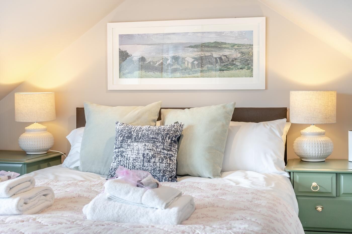 A neatly made bed with white linens, a patterned pillow, and a folded towel on a green nightstand.
