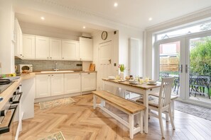 A modern kitchen with white cabinets, a wooden countertop, and a dining area with a bench and table. - 4 Bed in Mumbles (oc-g29069) (The Mumbles)