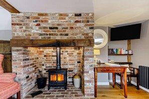 Ein gemütliches Zimmer mit Kamin aus Backsteinen, einem Holztisch, einem Bücherregal und einem bequemen Sessel.