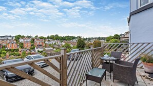 En balkon med fletmøbler, et bord og stole, med udsigt over et boligområde med biler og huse.