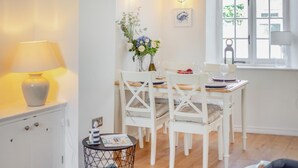 A dining area with a white table and chairs, a vase with flowers, a lamp, and a window with a view. - 2 Bed in Appledore (oc-m29918) (Appledore)