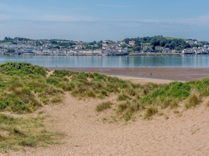 Eine Küstenansicht mit einem Sandstrand, grasbewachsenen Dünen und einer Stadt im Hintergrund.