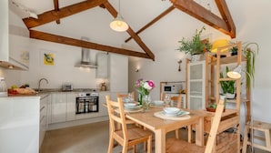 Une cuisine moderne avec des meubles blancs, une table à manger en bois et un four encastré.