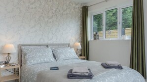 Quarto com cama, duas mesas de cabeceira, janela com cortinas e vista para o verde lá fora.