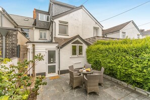 A residential property with a patio area featuring wicker furniture and a small table with a bottle and fruit. - 4 Bed in Bude (oc-s30486) (Bude)