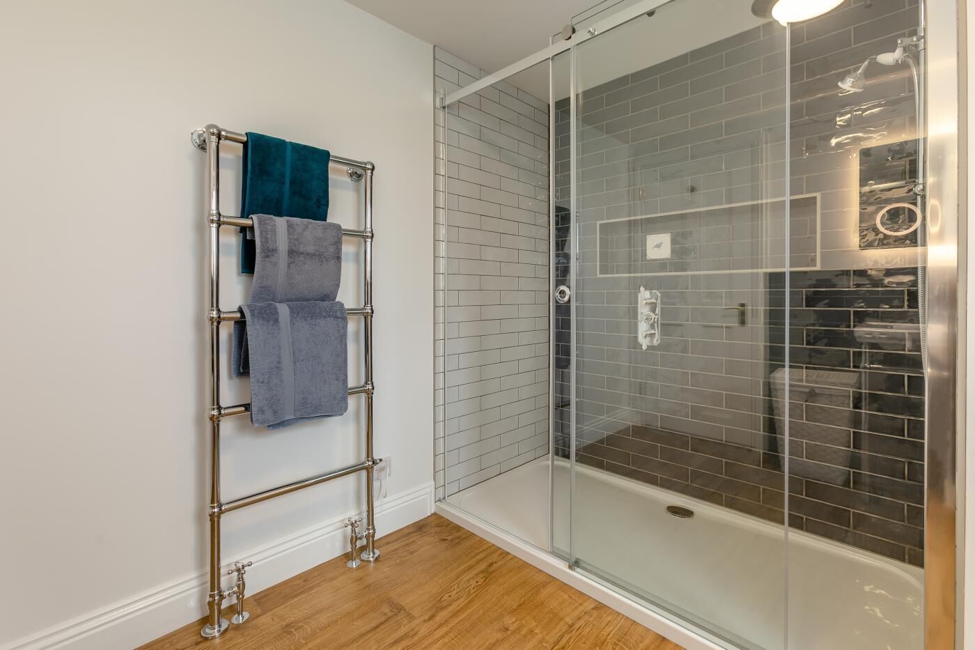 A bathroom with a glass shower enclosure, a towel rack with towels, and a wooden floor.