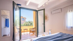 A bedroom with a bed, a small table with a bottle, a chair, and a balcony with a view of a building and trees. - Just 50 steps from the beach: Vacation Home for 9 Guests & BBQ (Mandriola)
